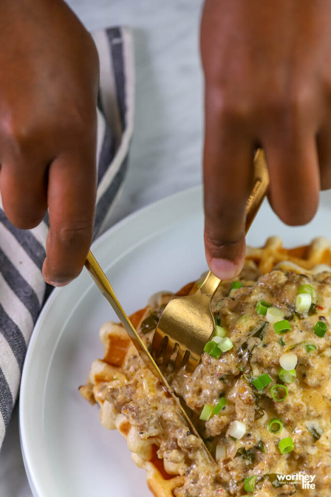 hands cutting into waffles with sausage gravy