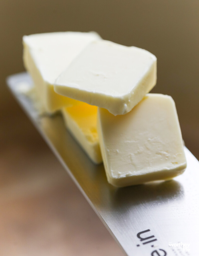 Several pats of unsalted butter on the side of a knife. 